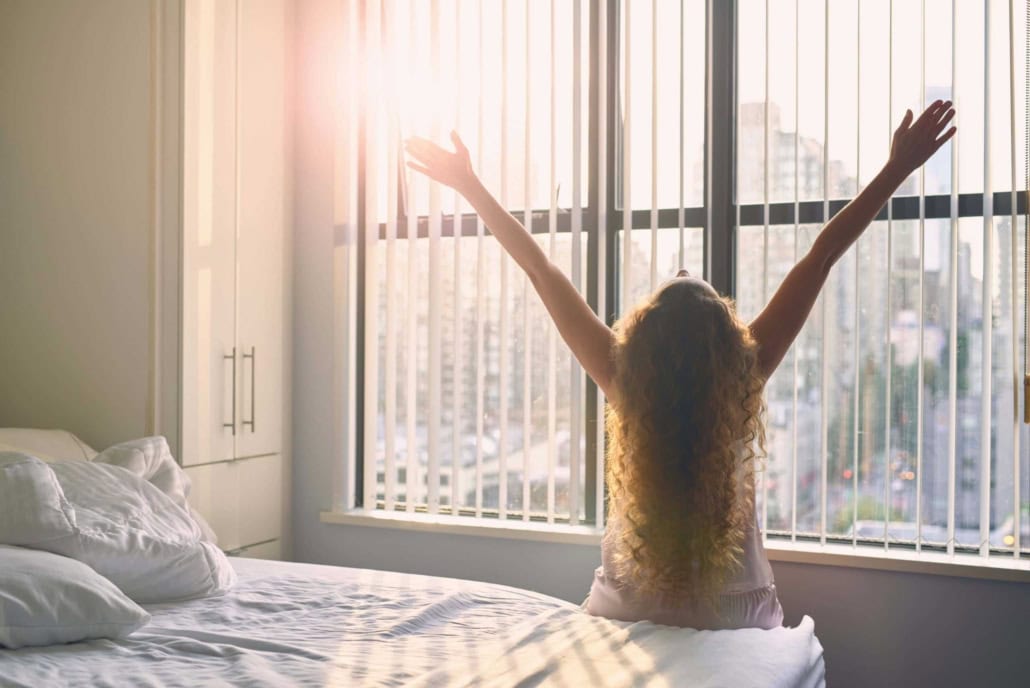 Frau begrüßt den Morgen am Fenster