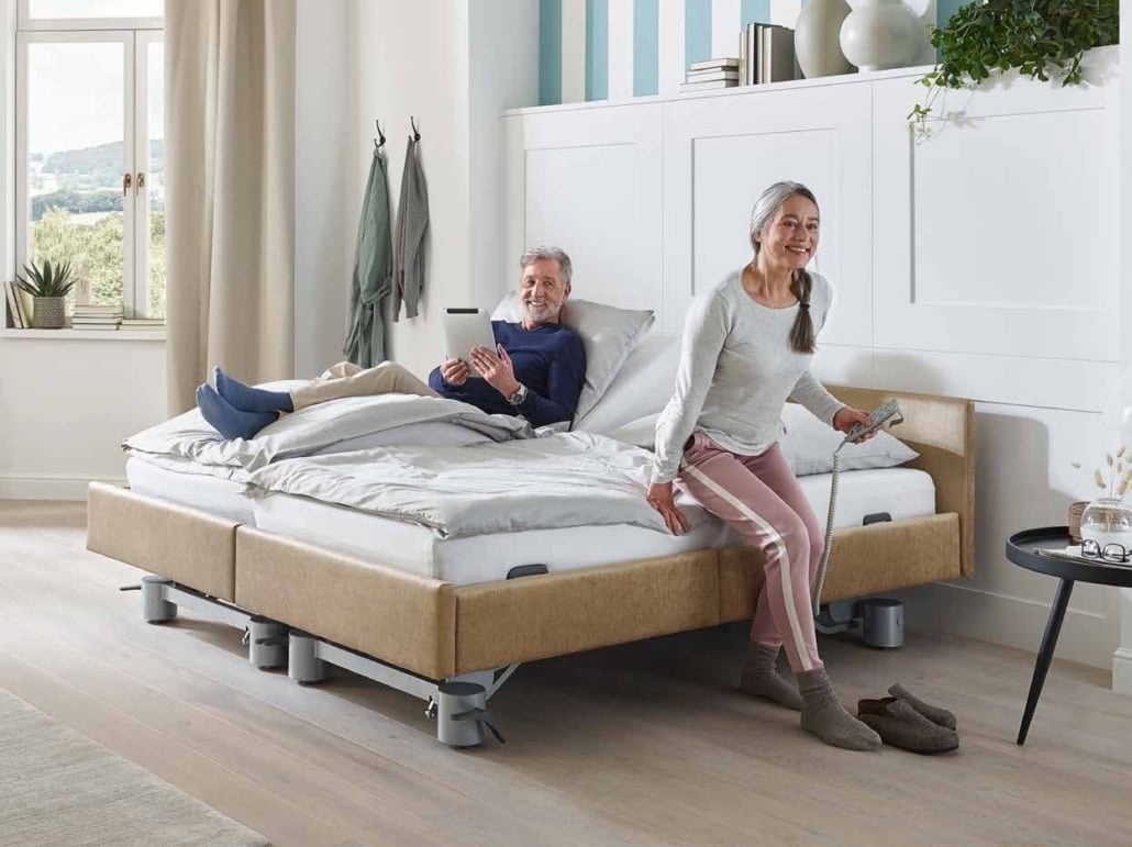 Paar sitzt aufrecht im Stiegelmeyer Libra Partnerbett mit beidseitig verstellbaren Rückenlehnen, Holzdekor Buche
