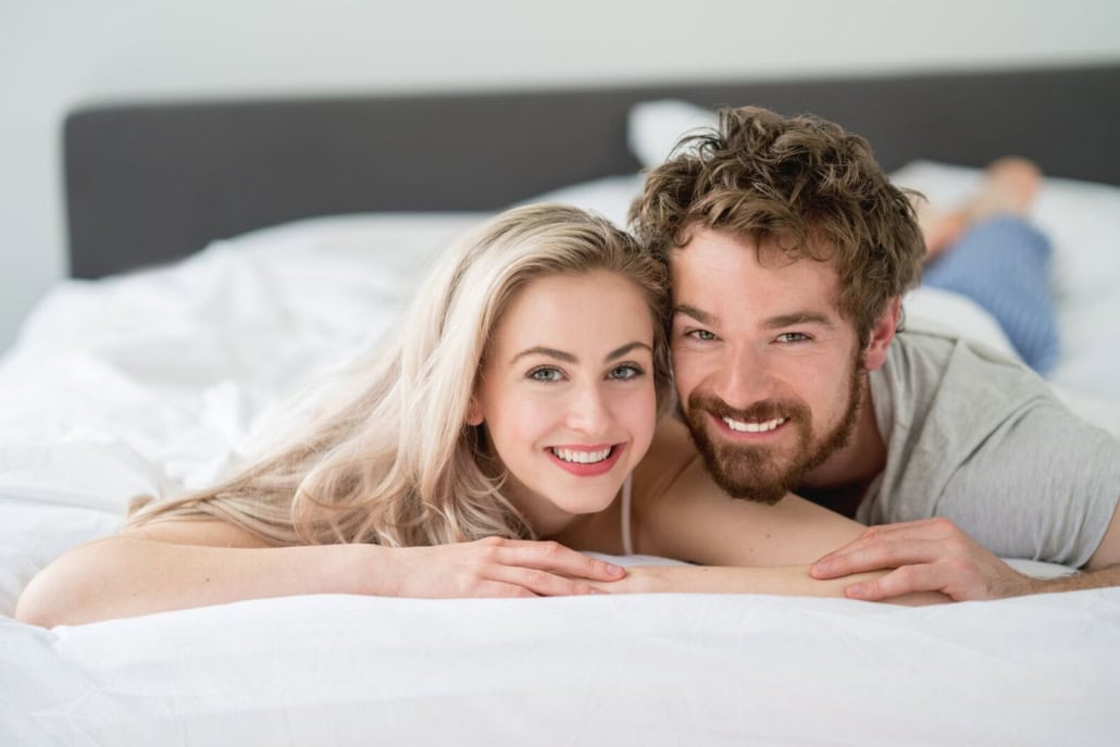 Paar liegt auf dem Bett und lächelt